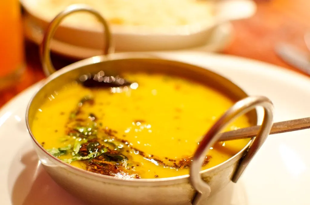 A small bowl of yellow dal with a tadka of spices and curry leaves on top