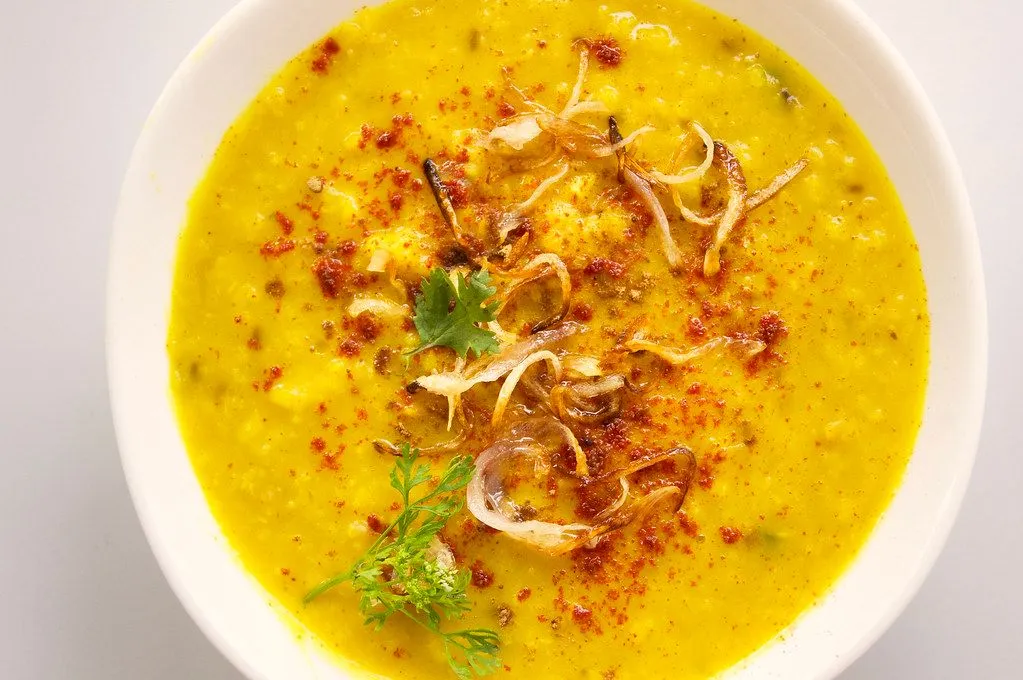 A bowl of yellow dal topped with fried onions, chilli powder and coriander