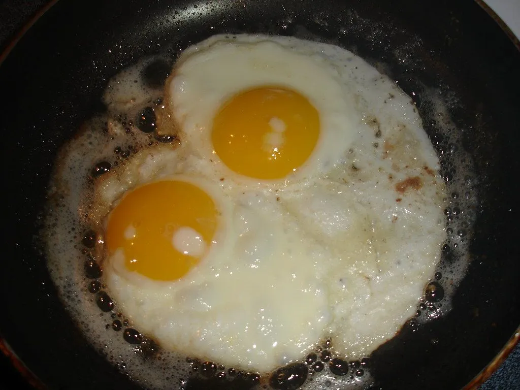 Two eggs frying in butter in a dark pan