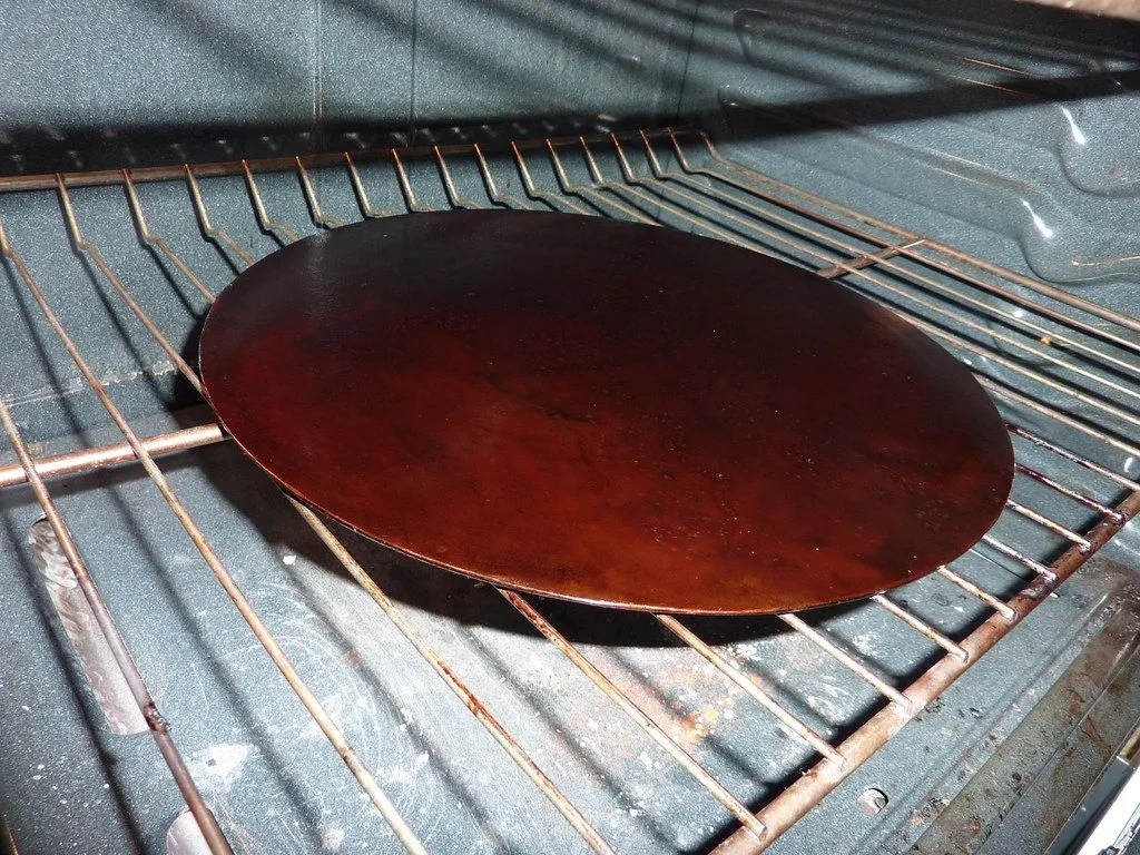 A round cast iron crepe pan with a first coat of baked-on oil, resting on an oven rack