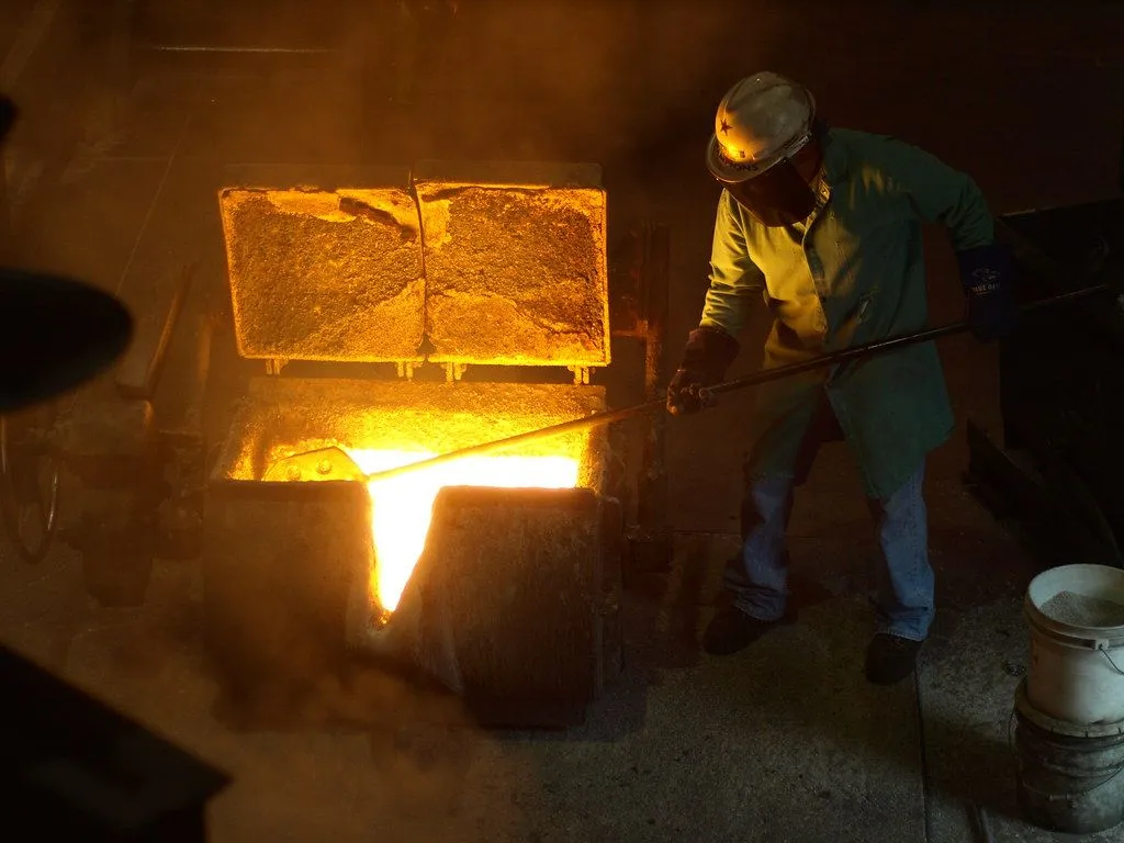 A foundry worker with a long rod standing beside a furnace full of glowing molten metal