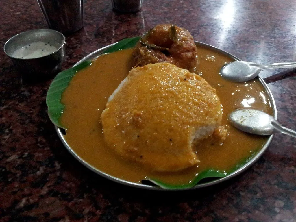 An idli and a vada covered in orange sambar on a plate lined with a banana leaf