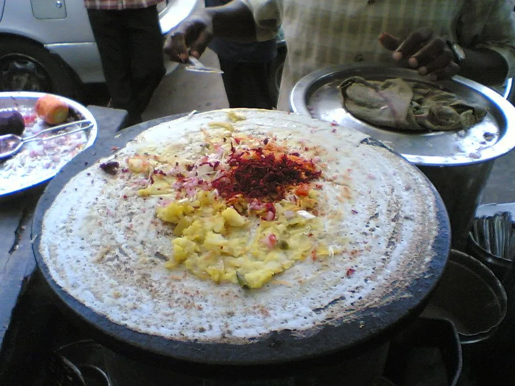 A masala dosa on a large dark flat griddle, with potato filling and chutney powder