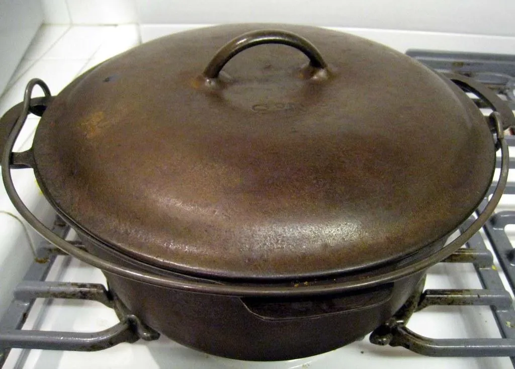 An old cast iron Dutch oven with its lid on, sitting on a gas hob