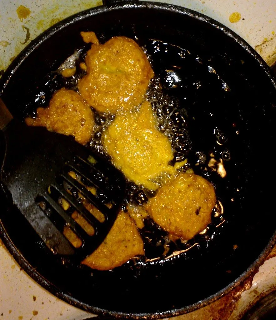 Pakoras frying in a black pan, with bubbling oil around them