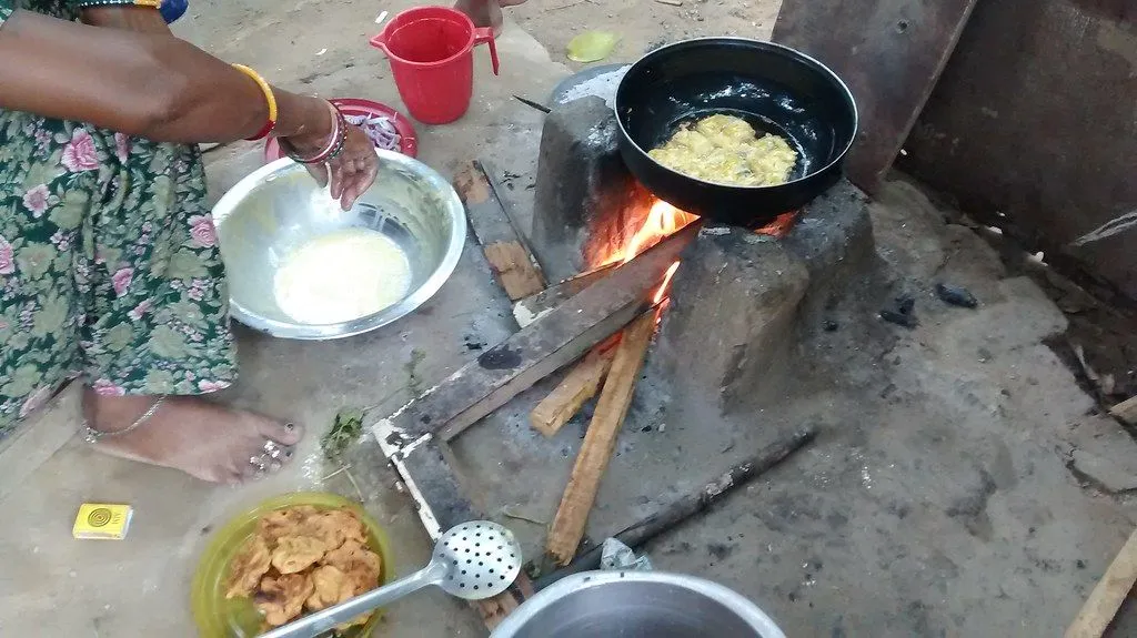 A cooking vessel over a wood fire with pakora batter frying in oil