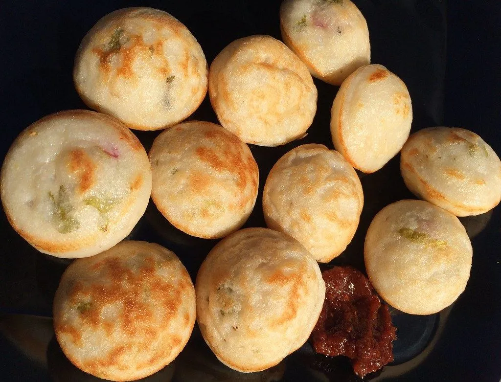 A plate of golden paniyaram balls, some with green chilli and onion visible