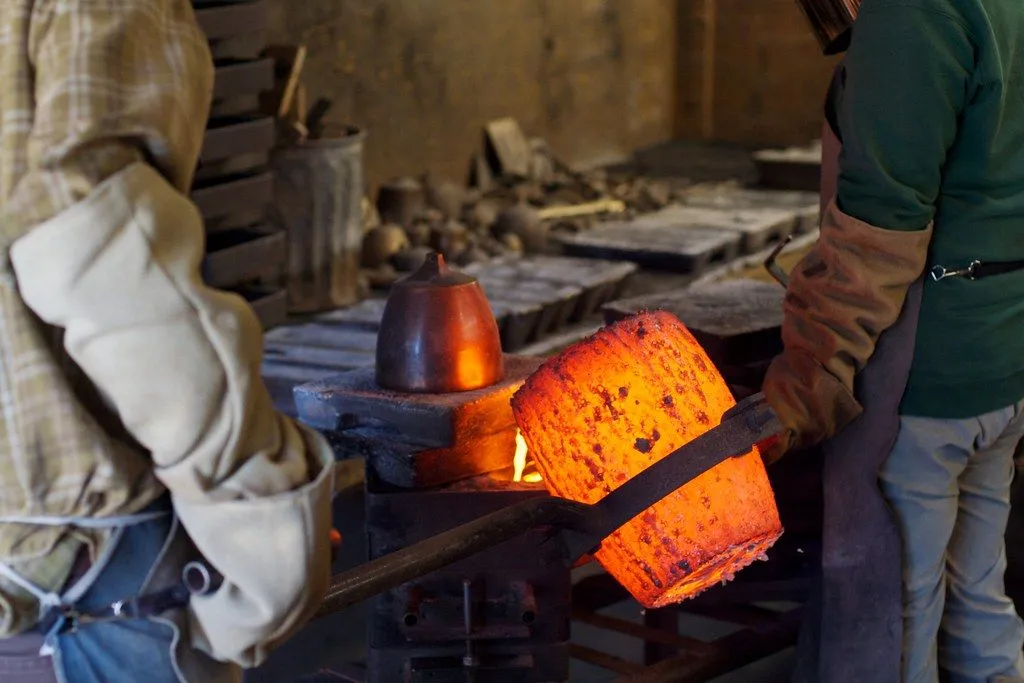 A foundry worker tilting a glowing ladle to pour molten metal into a mould