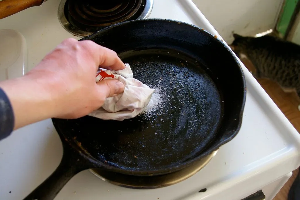 Coarse salt being rubbed on a cast iron pan with a cloth to loosen stuck food
