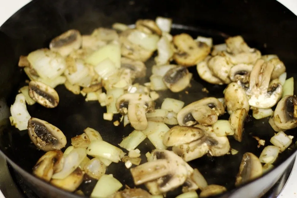 Chopped onions and mushrooms sautéing in a dark pan
