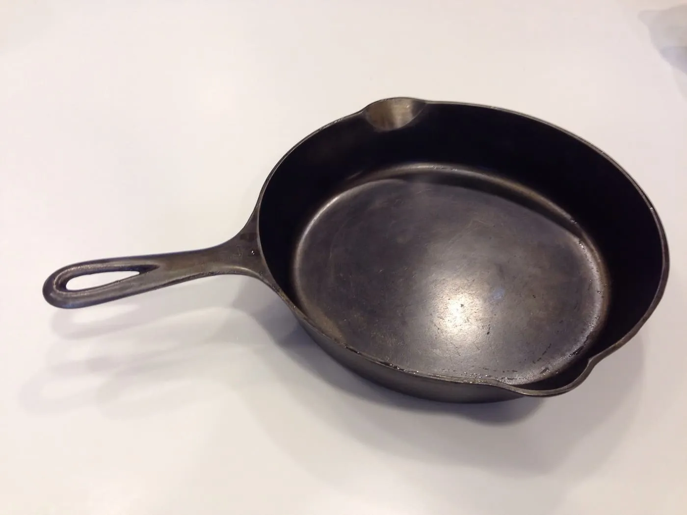 The inside of a cast iron pan with a dark, partly shiny seasoned surface