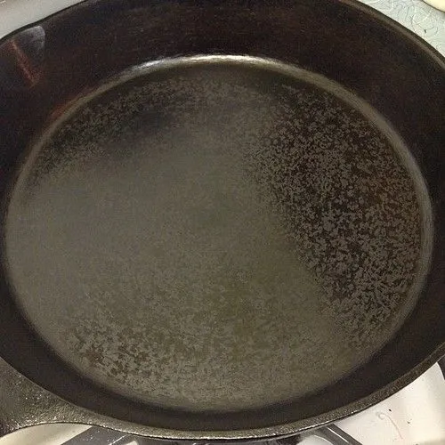 The inside of a cast iron pan with a dark, partly shiny seasoned surface