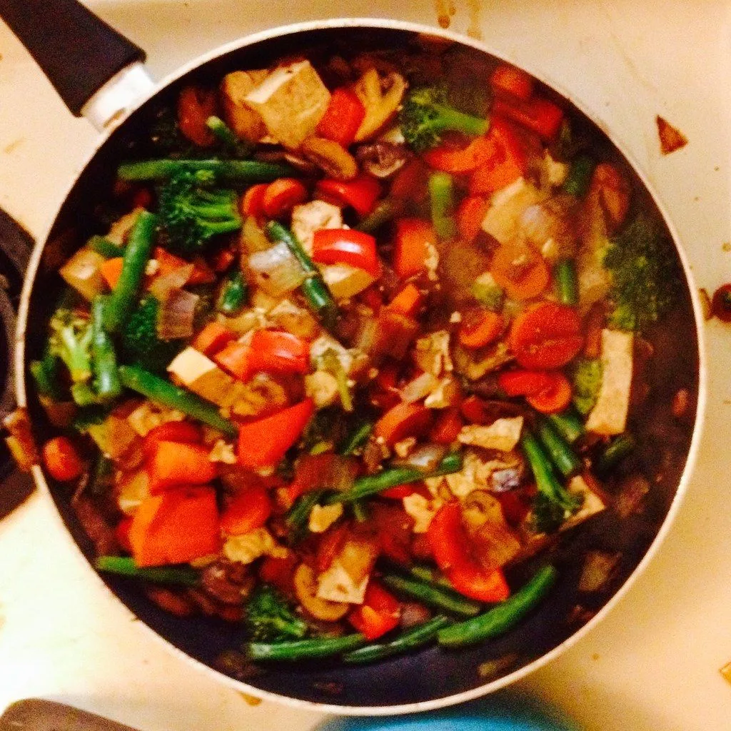 A vegetable stir-fry cooking in a dark-coated pan on a home stove