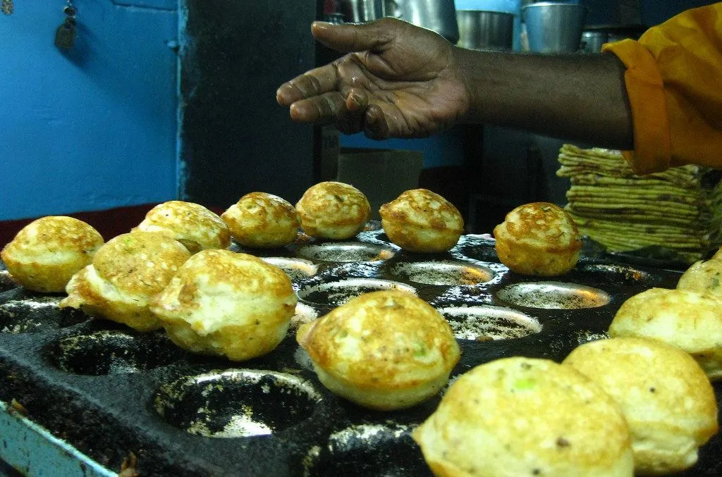 A cook tending paddu in a pan with deep round pits, golden brown and cooked on both sides