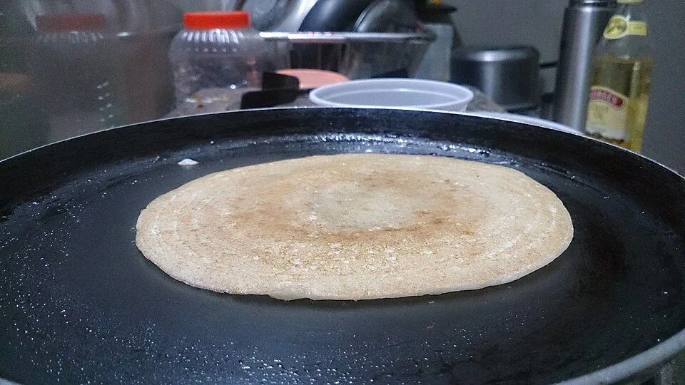A dosa cooking on a large round dark tawa