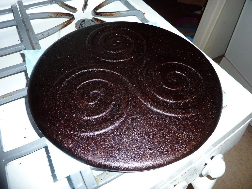 A dark, glossy, evenly seasoned round cast iron pan on a gas stove after its third coat of oil