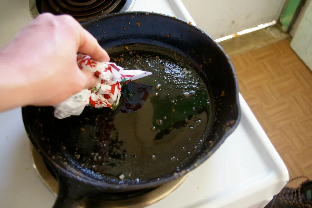 A cook wiping a used cast iron pan with a paper towel while it is still warm