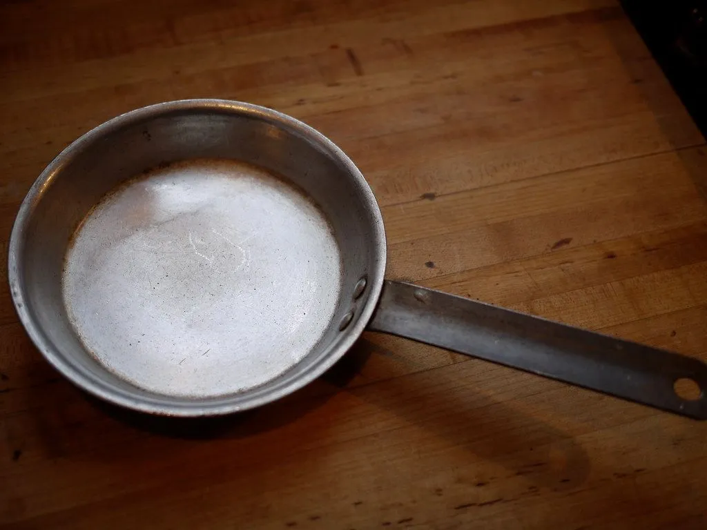 A worn, scratched metal frying pan with a dull, marked cooking surface