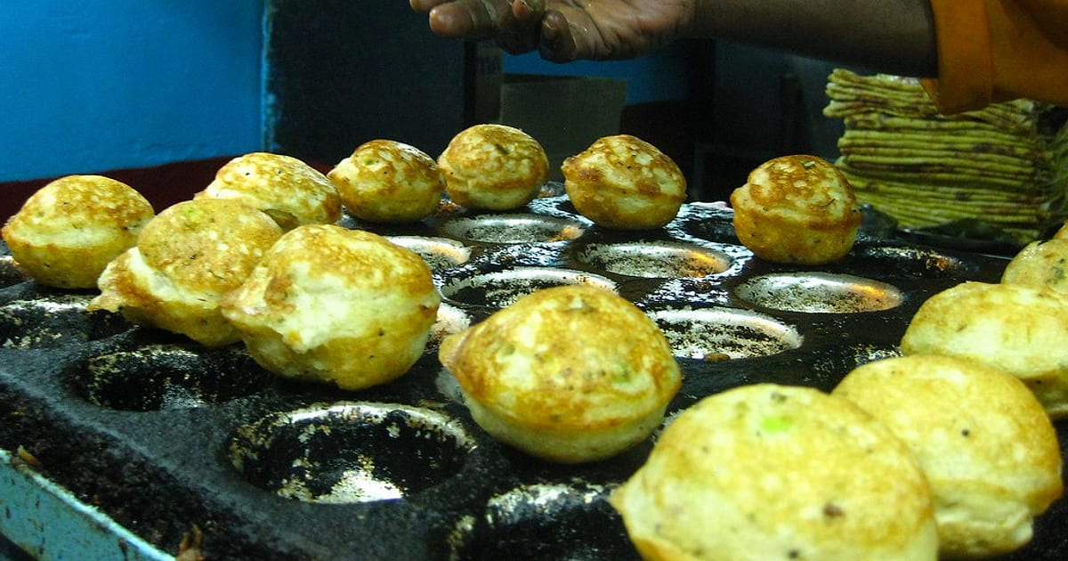 Golden kuzhi paniyaram cooked in a large cast iron appe pan at a street stall