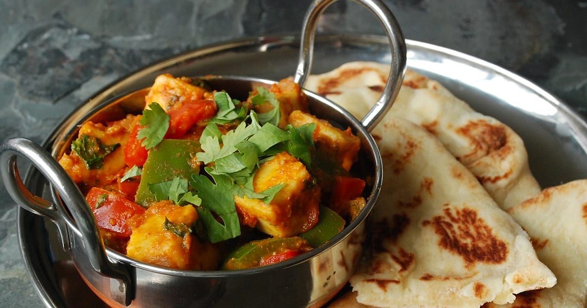 Kadai paneer with peppers, tomato and fresh coriander in a small kadai, with naan on the side