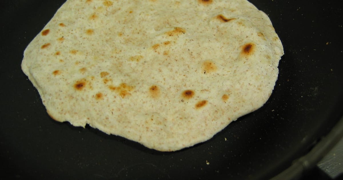 A fresh chapati with golden-brown spots cooking on a dark iron tawa