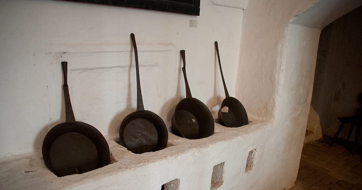 Four long-handled iron pans in four sizes resting in the openings of an old whitewashed stove
