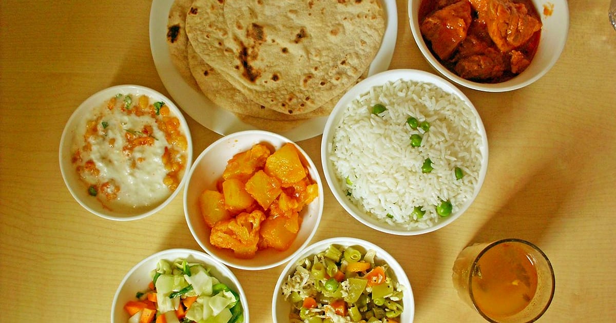 A home-cooked Indian meal from above: rotis, aloo gobi, peas pulao, raita, mixed vegetables and curry in white bowls