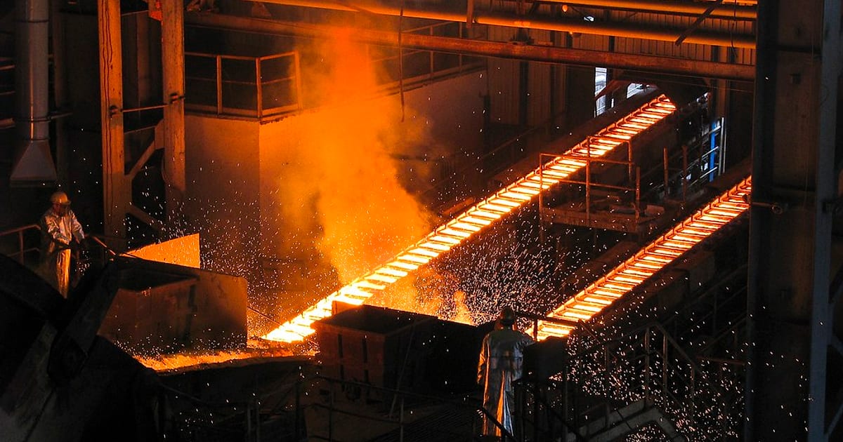 Glowing molten metal running down channels in a foundry, with sparks flying and workers in heat-proof suits