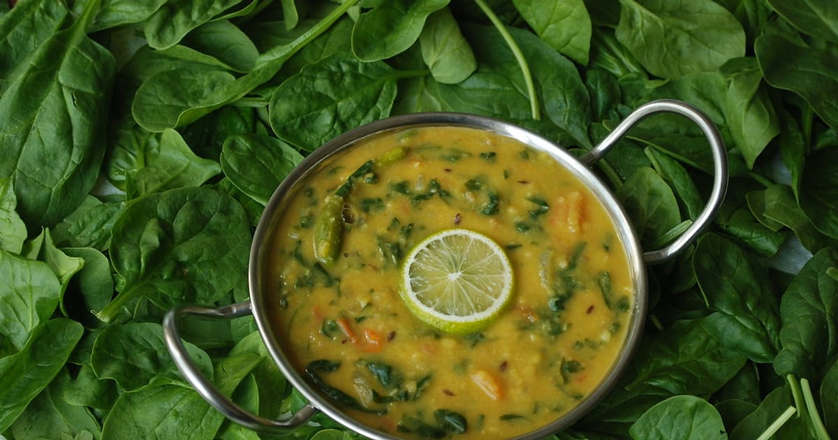 Dal palak — spinach and lentil curry with a slice of lime — in a small kadai on a bed of fresh spinach leaves