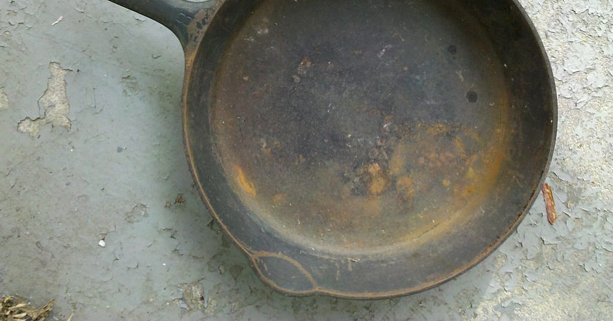 An old cast iron skillet with orange rust patches across its cooking surface, waiting to be restored