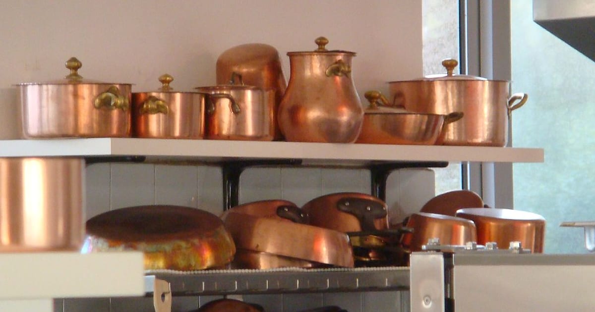 Shelves of gleaming copper pots, pans and lids in a restaurant kitchen